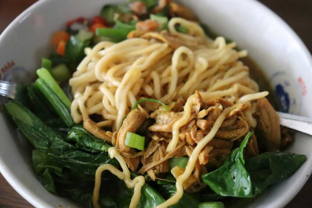 Semangkuk mie ayam dengan topping ayam dan sawi hijau