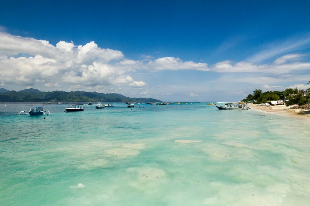 Pantai Gili Trawangan dengan air laut jernih, perahu wisata, dan latar perbukitan Lombok