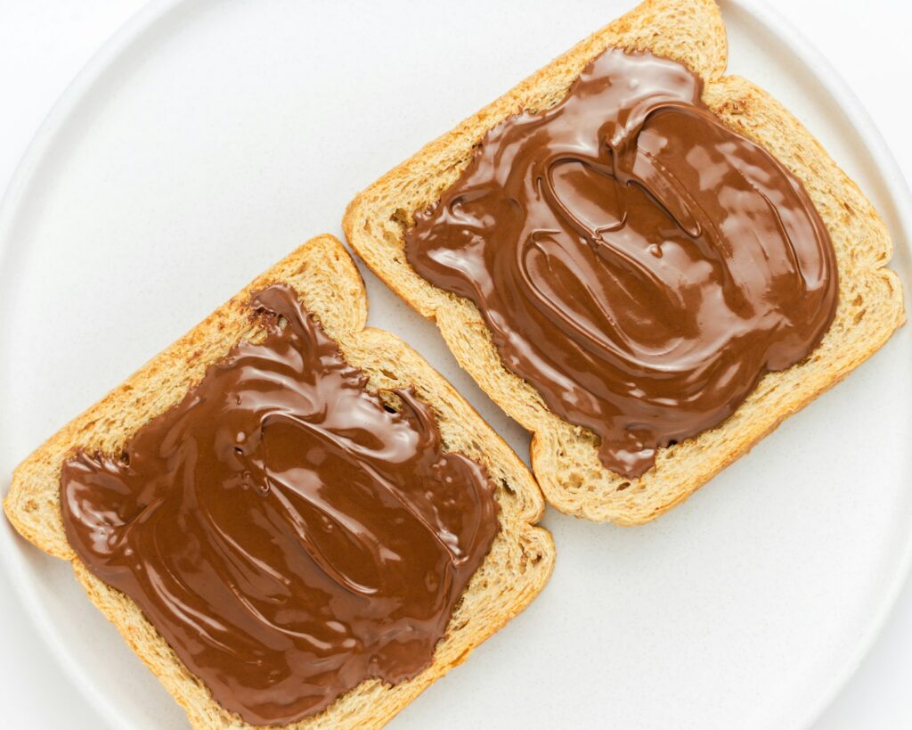 Roti bakar dengan olesan cokelat di atas piring putih